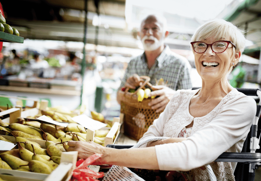 Dieses Bild zeigt eine ältere Dame im Rollstuhl an einer Obstheke im Supermarkt