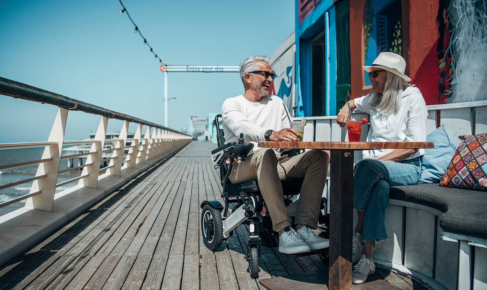 Dieses Bild zeigt einen Mann in einem faltbaren E-Rollstuhl, der in einem Restaurant am Meer sitzt