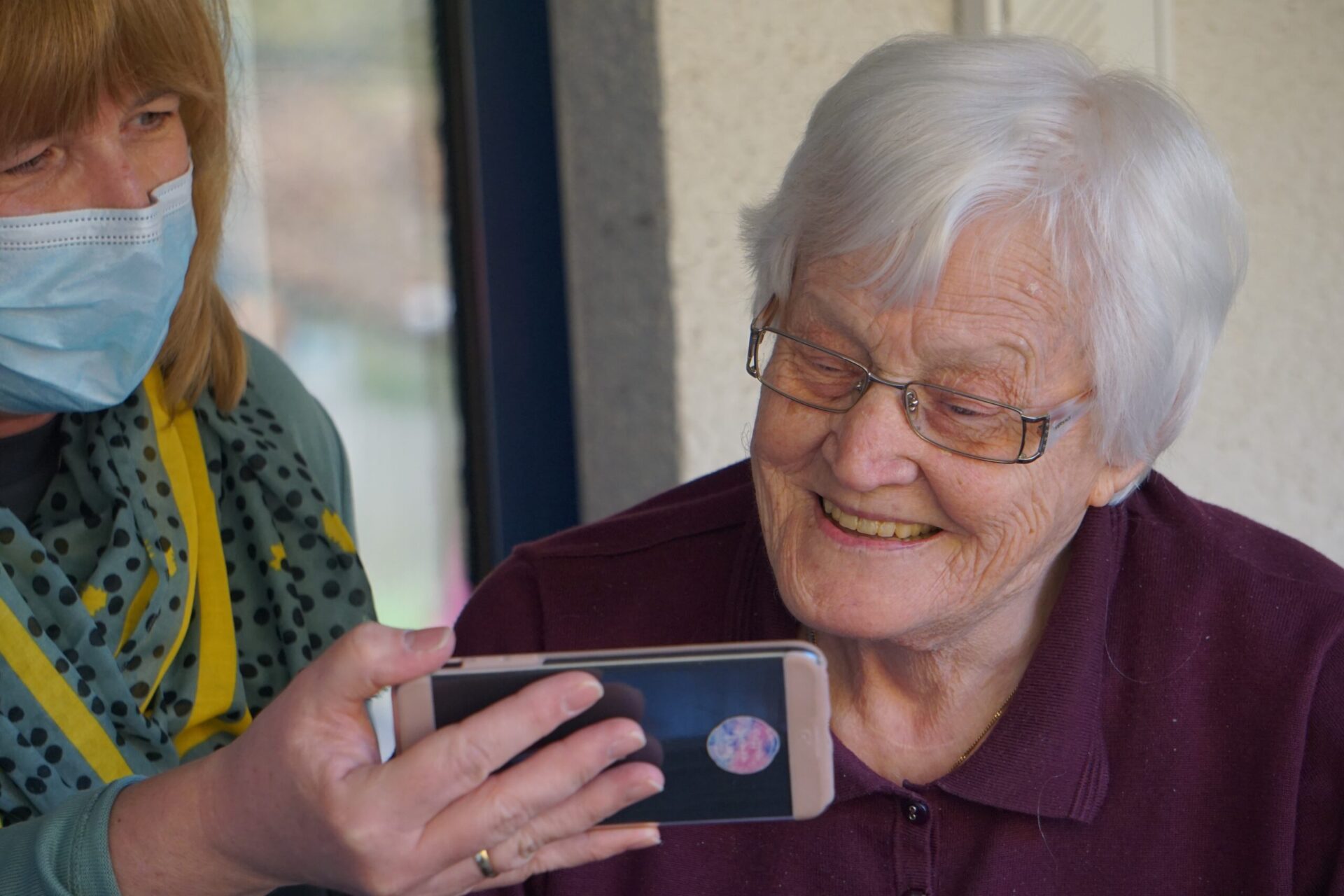 Dieses Bild zeigt eine ältere Dame, der gerade was auf einem Handy gezeigt wird als Symbolbild für Angehörige pflegen