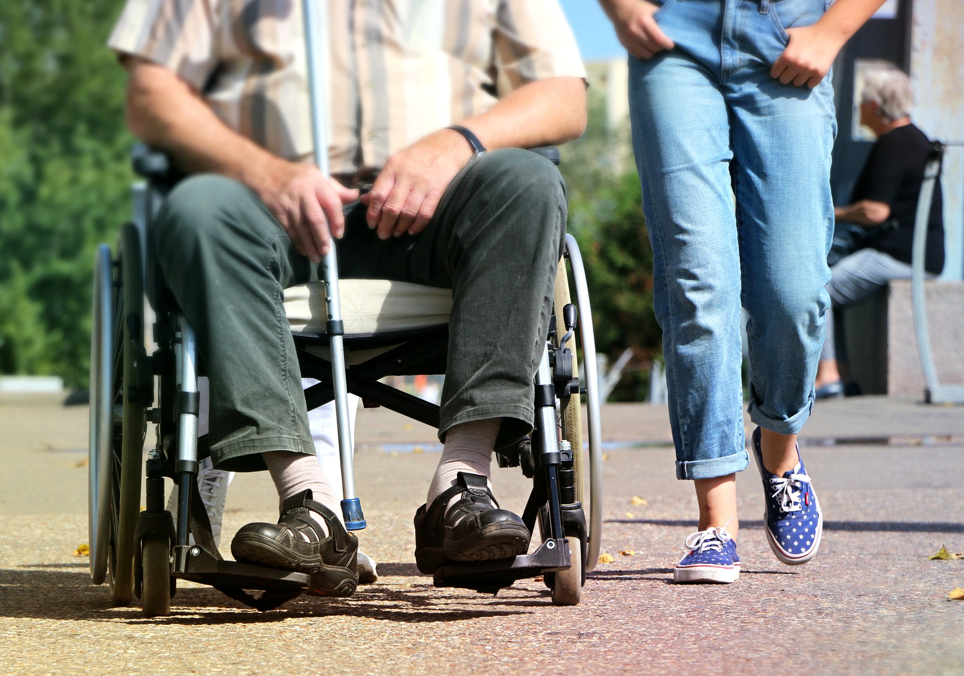 Rollstuhl Pflegegrad 3: Auf dem Bild ist ein Mann im Rollstuhl zu sehen und daneben läuft eine Person.